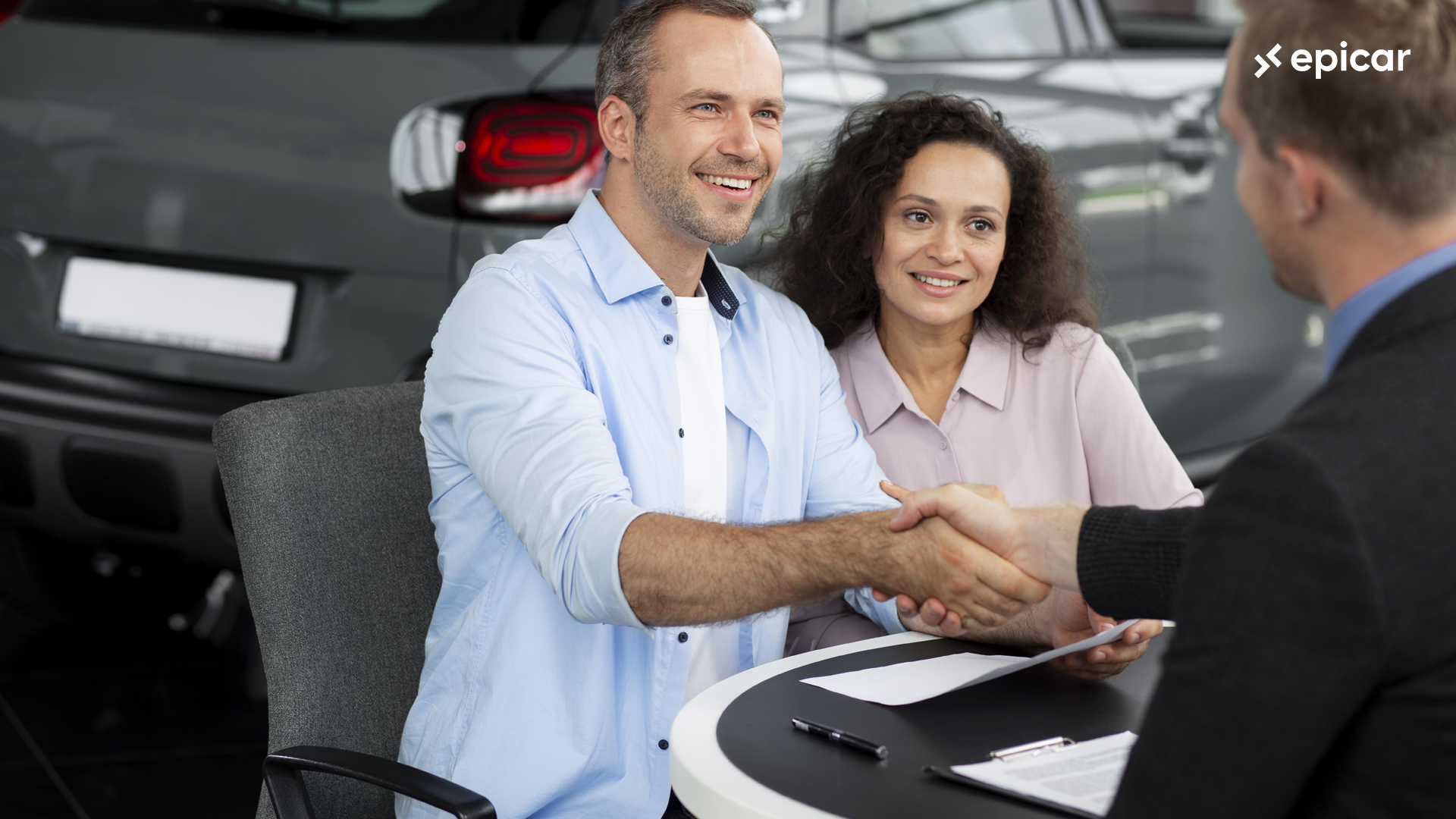 A seller and buyer exchanging paperwork with cash and a car in the background.
